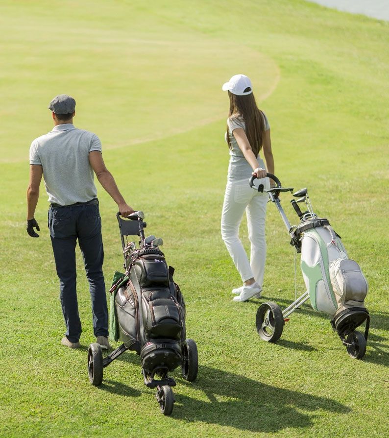 A man and a woman are pushing golf carts on a golf course.
