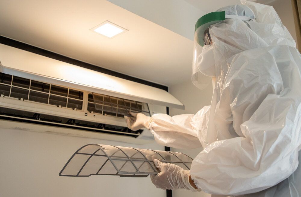Person in Protective Suit Cleaning an Air Conditioner Filter — Hinterland Air Conditioning Sunshine Coast in Palmwoods, QLD