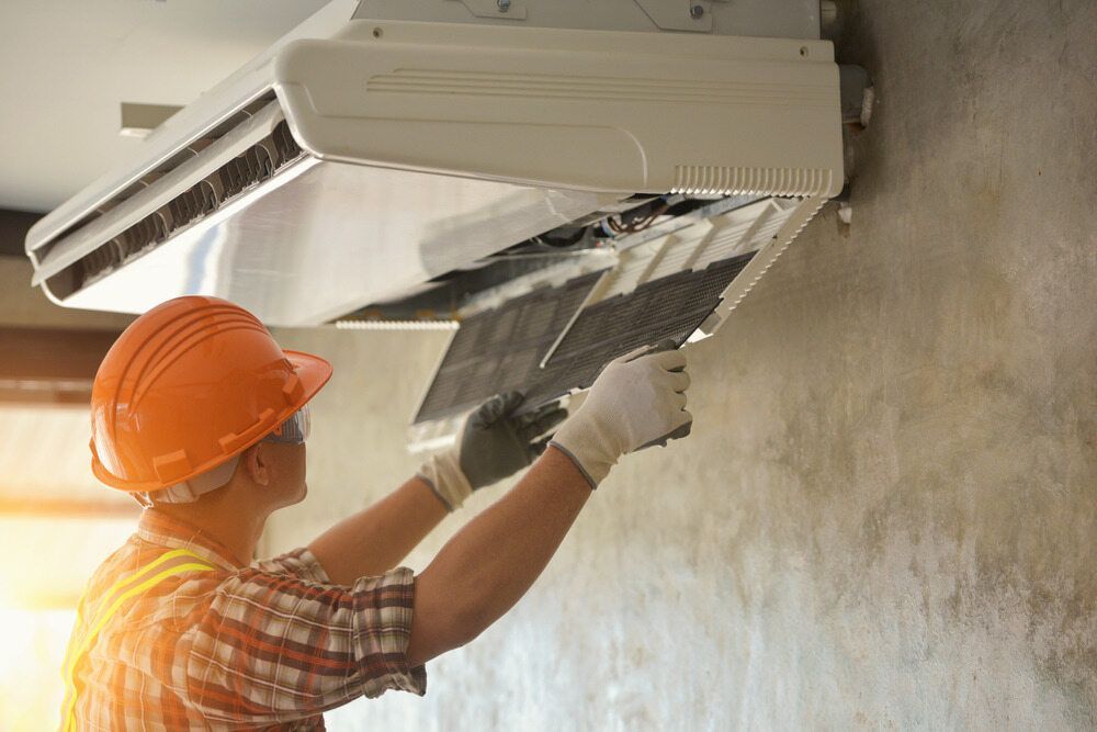 Technician Cleans an Air Conditioner Filter on a Concrete Wall — Hinterland Air Conditioning Sunshine Coast in Palmwoods, QLD