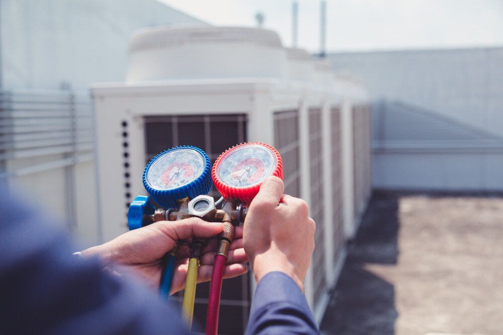 Hands Holding Gauges in Front of an Air Conditioning Unit — Hinterland Air Conditioning Sunshine Coast in Palmwoods, QLD