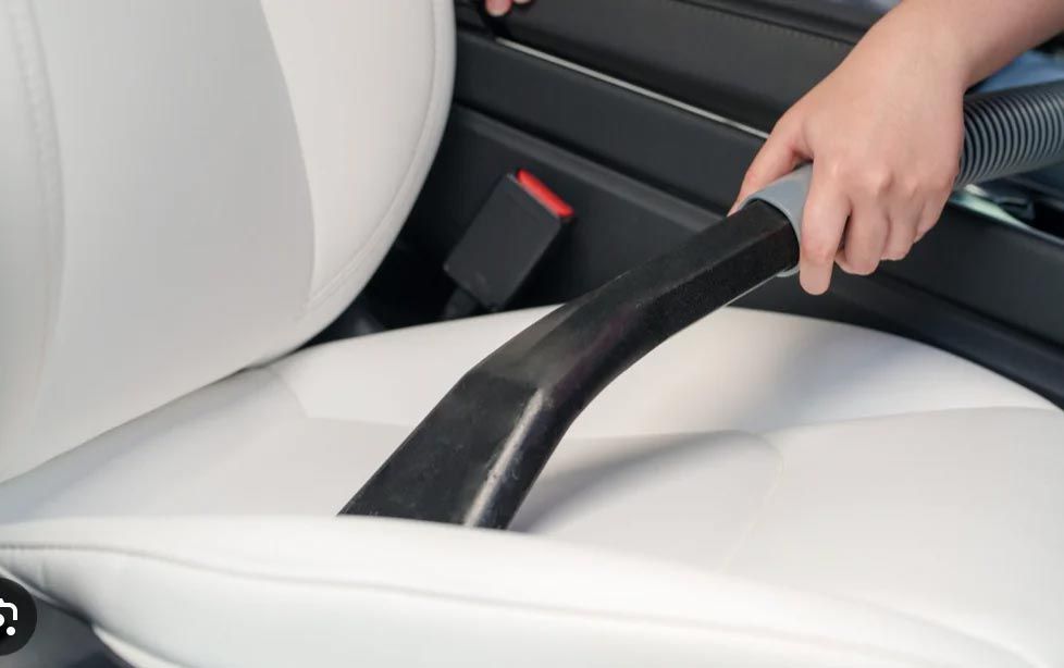 Hand using a black car seat gap cleaner between white leather seats