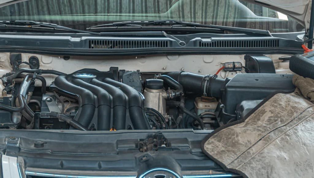 Open car engine bay with black intake manifold and dusty components under the hood.