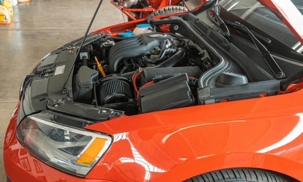 Close-up of a red car with its hood open, showing the engine in a garage.