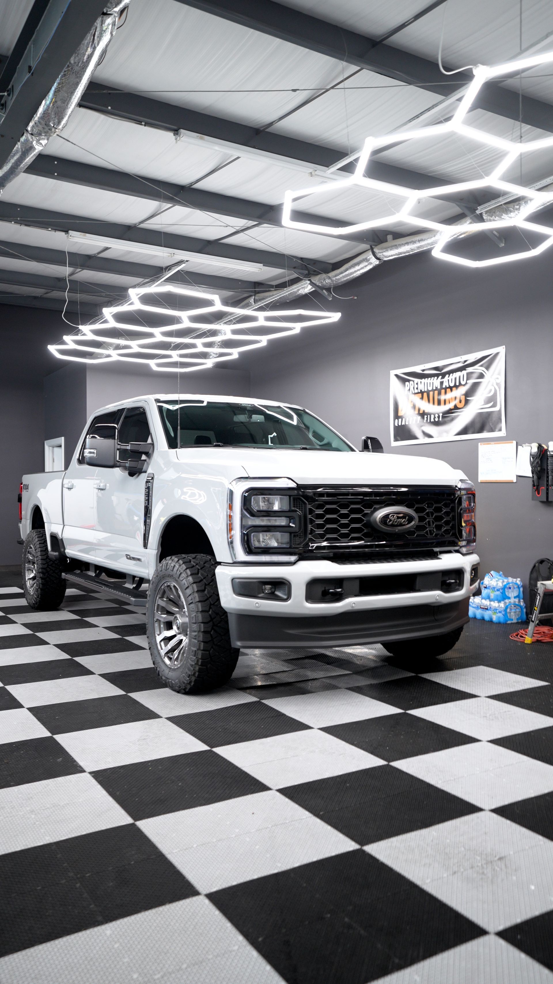White pickup truck in a modern garage with black-and-white checkered floor and hexagonal ceiling lights