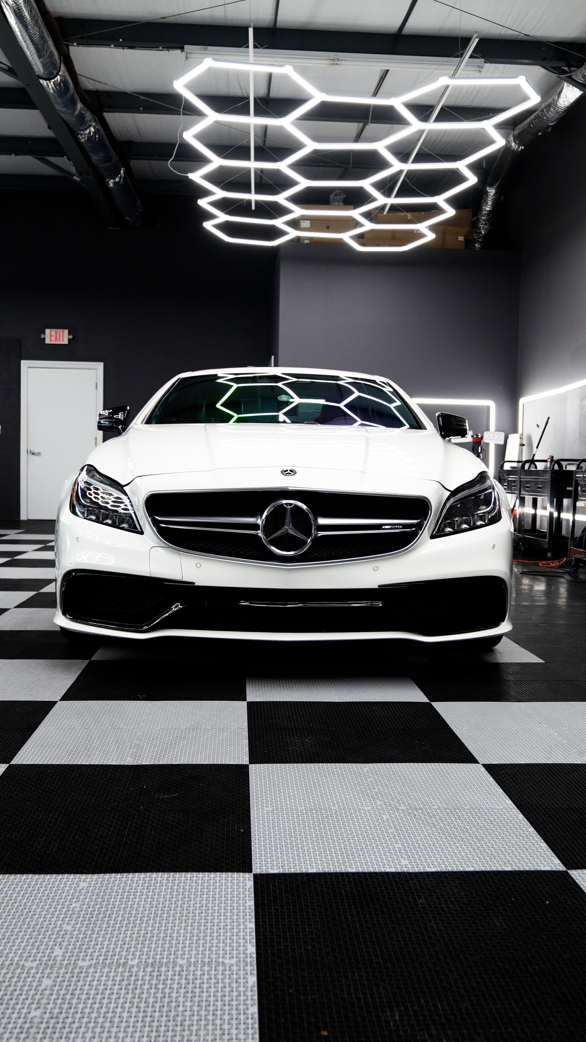White Mercedes-Benz sedan in a showroom with geometric ceiling lights and a black-and-white checkered floor