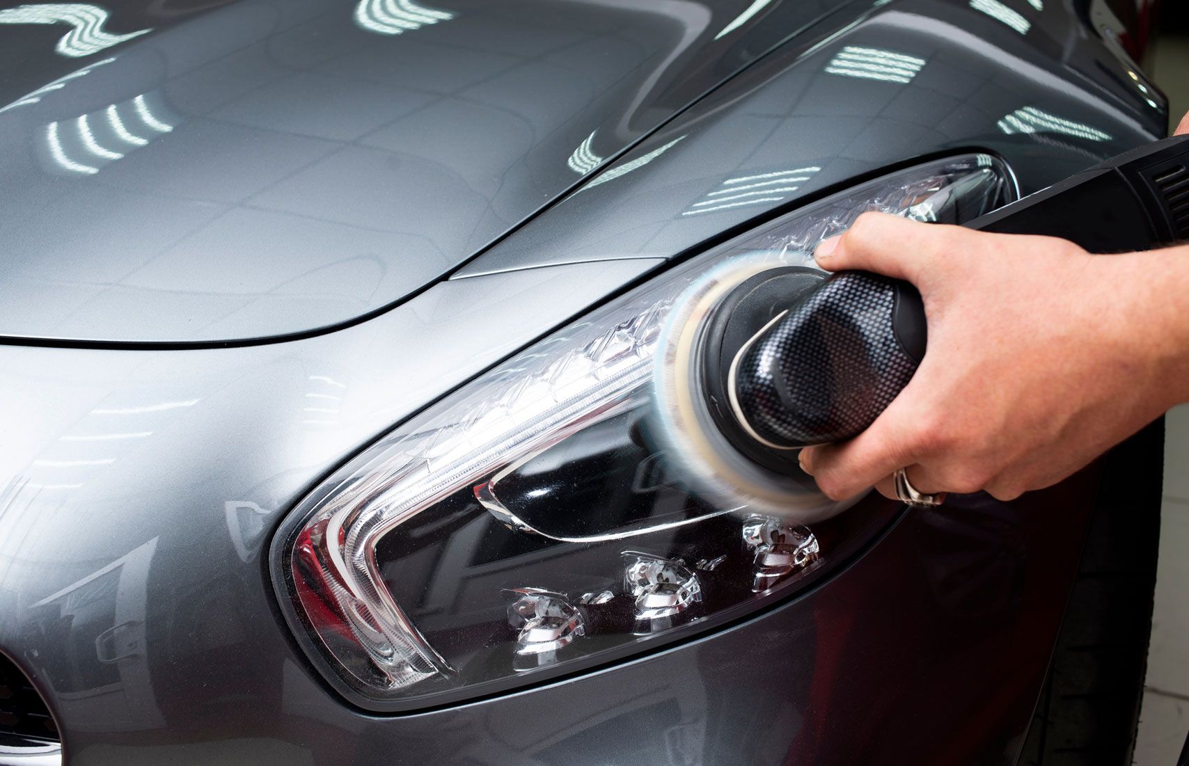 Person polishing a dark car headlight with a cloth