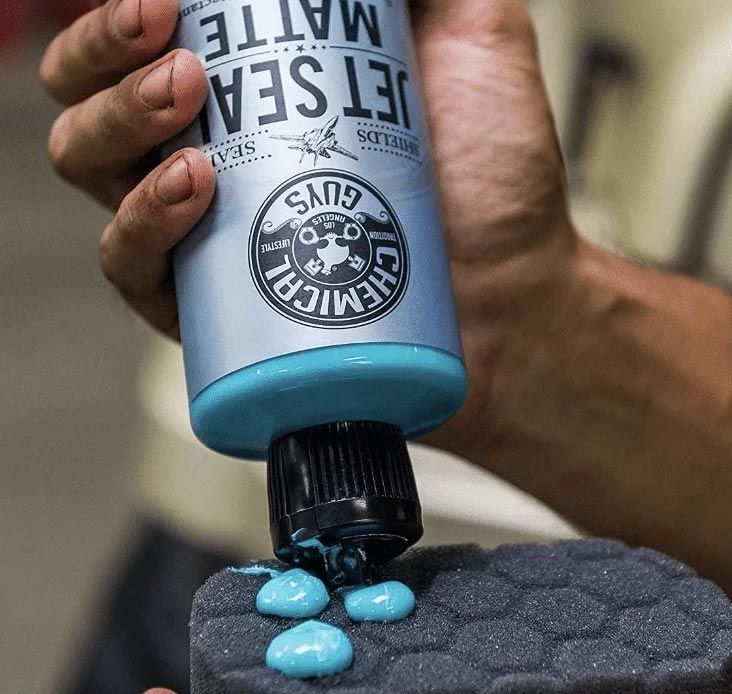 Blue lotion bottle dispensing drops onto a textured black surface