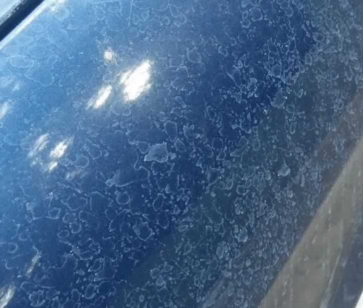 Close-up of a blue car hood with white water spots and reflections