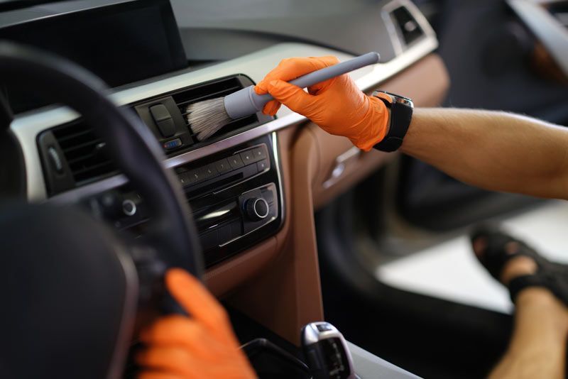 Gloved hands cleaning a car dashboard with a cloth and spray bottle