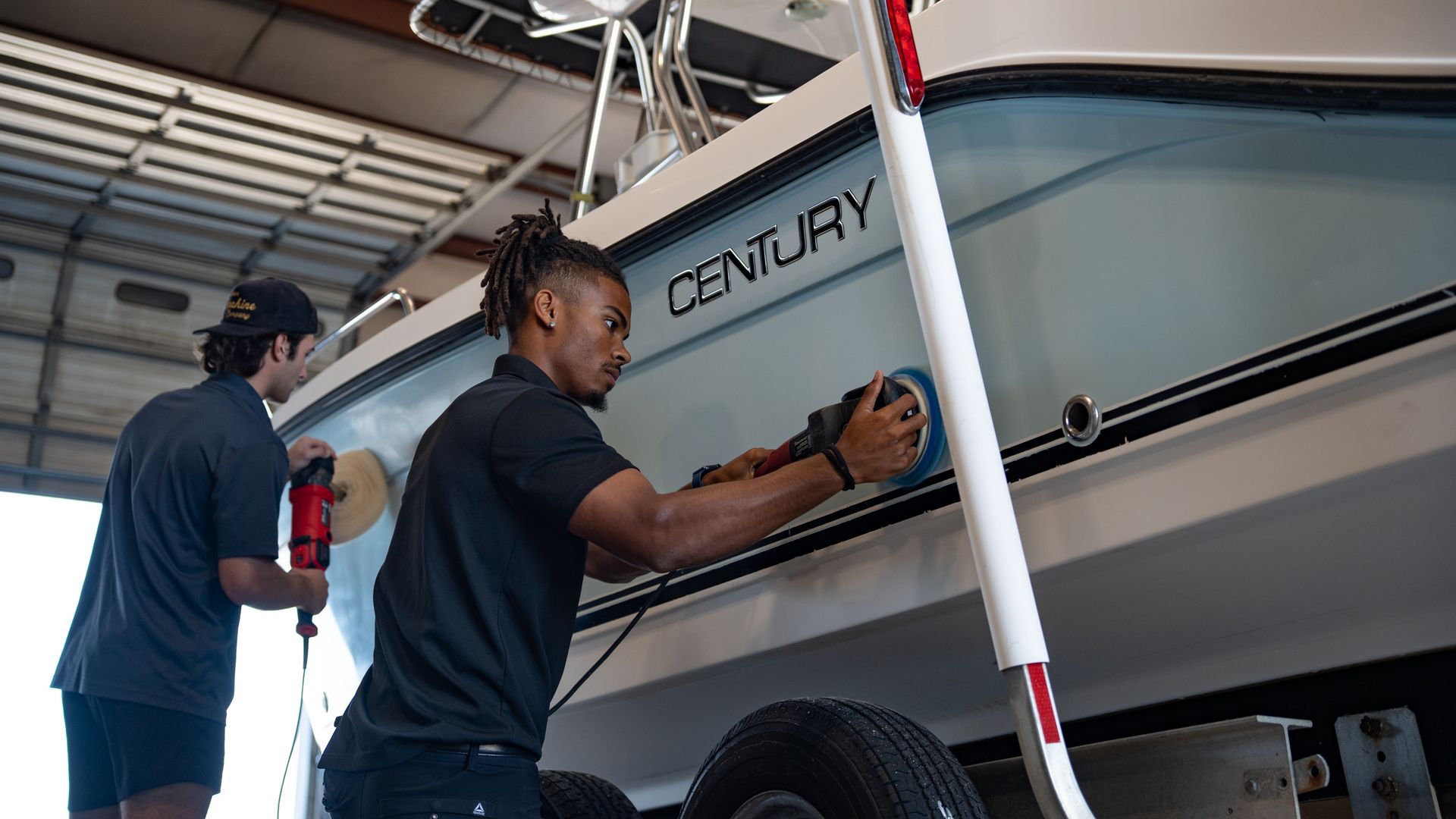 Two people cleaning a white Century boat in a covered garage