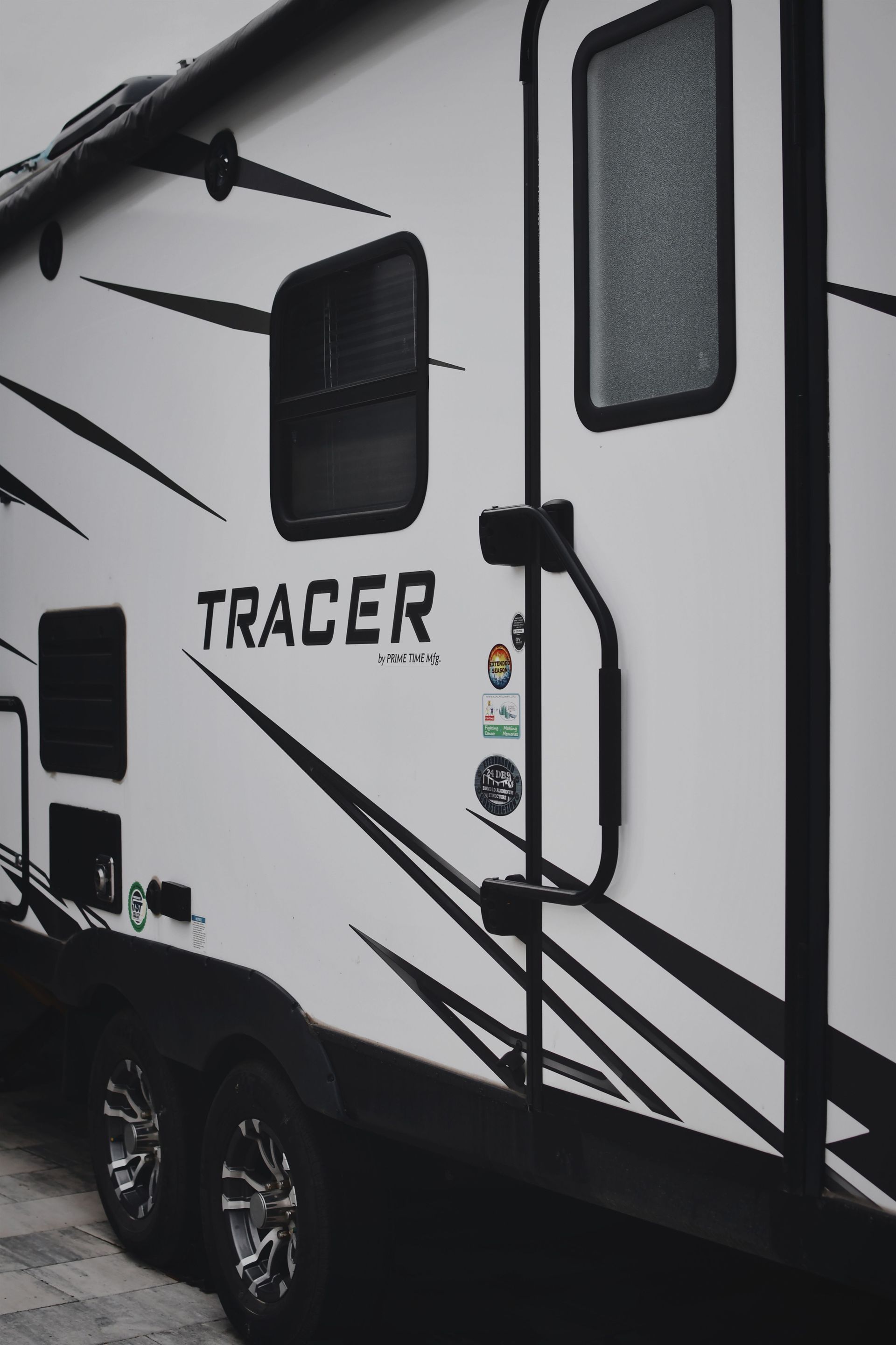 White Tracer travel trailer with black stripes and windows, shown from the side.