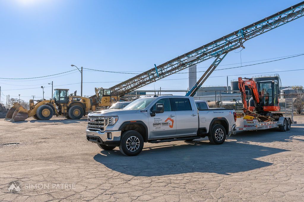 Un camion blanc remorque une grande pelle sur une remorque.