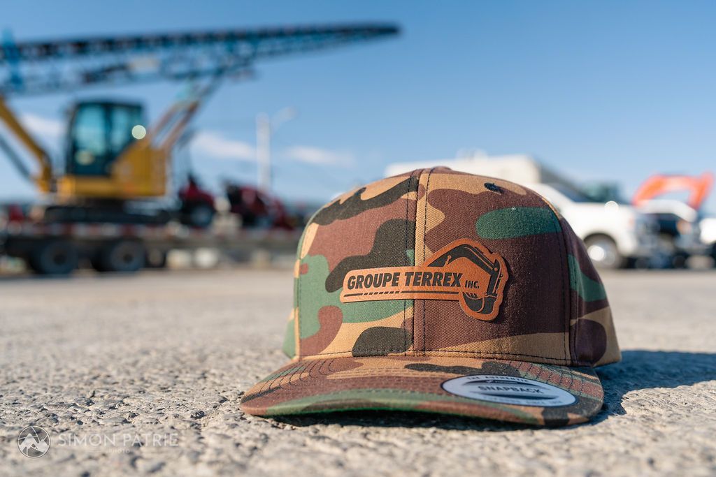 Un chapeau de camouflage est posé sur le sol devant un véhicule de construction.