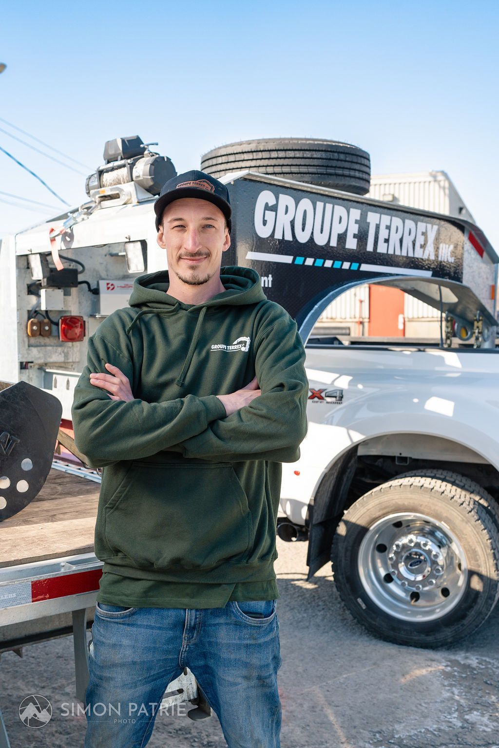 Un homme se tient devant une dépanneuse, les bras croisés.
