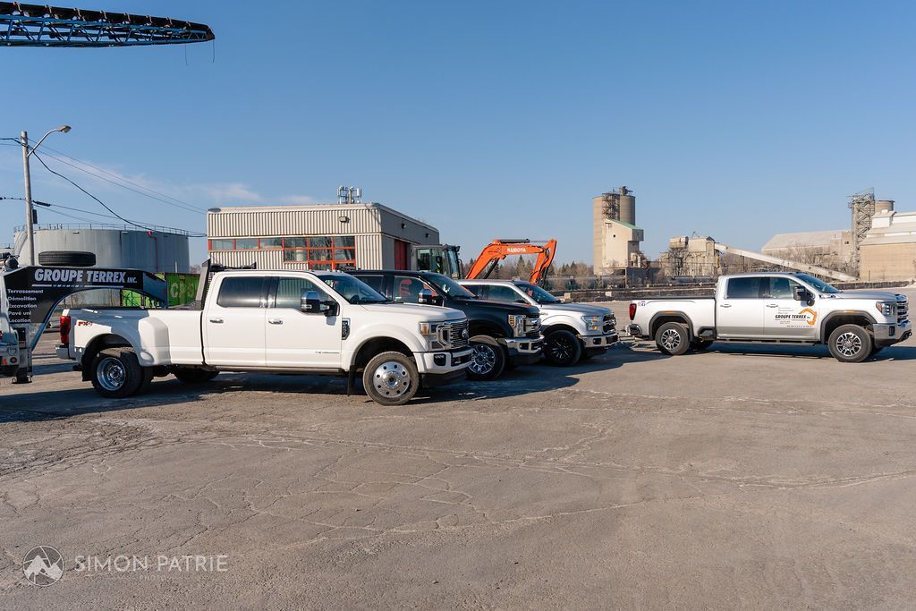 Une rangée de camions blancs sont garés dans un terrain sale.