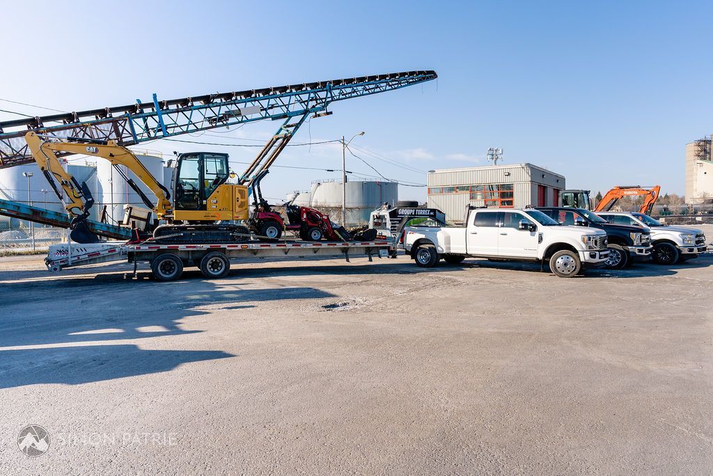 Un camion transporte une grue sur une remorque dans un parking.