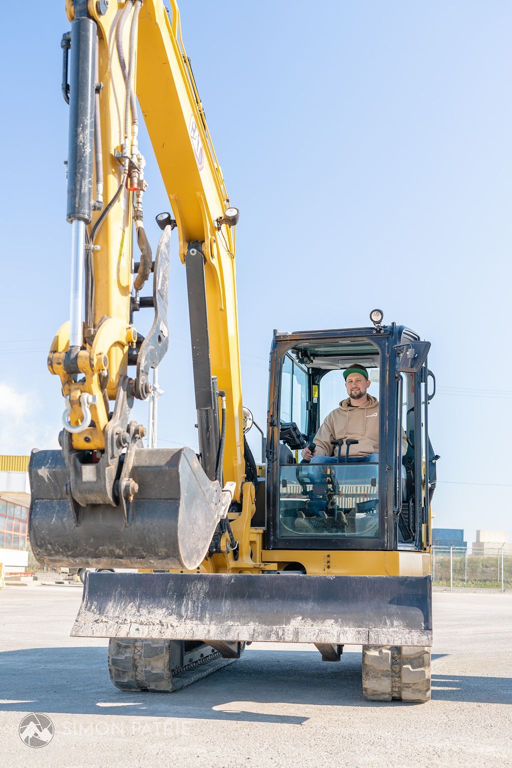 Un homme conduit une excavatrice jaune sur un parking.