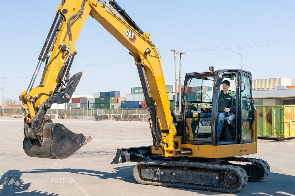 Un homme conduit une pelle jaune dans un parking.