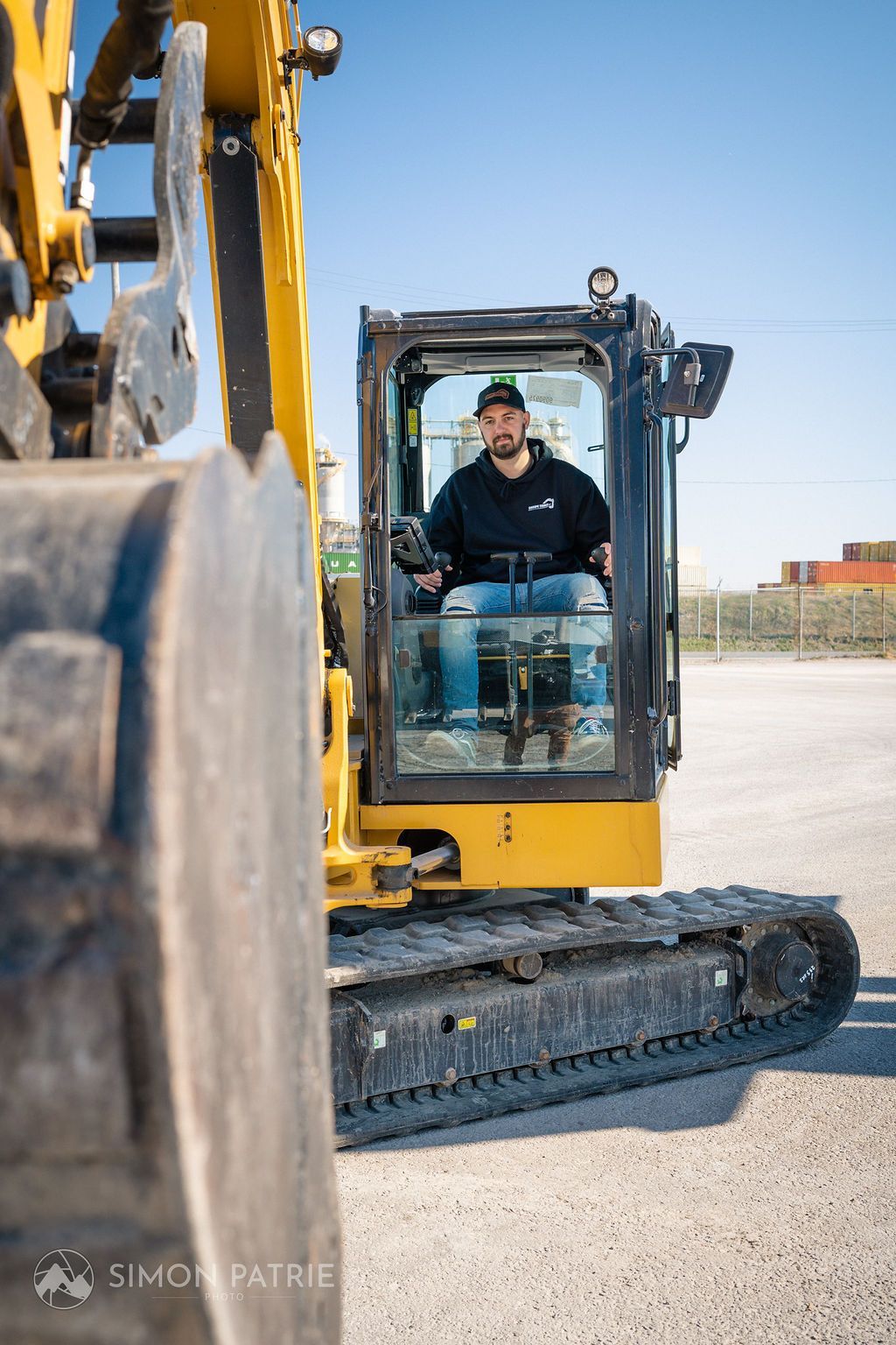 Un homme conduit une excavatrice jaune sur un parking.