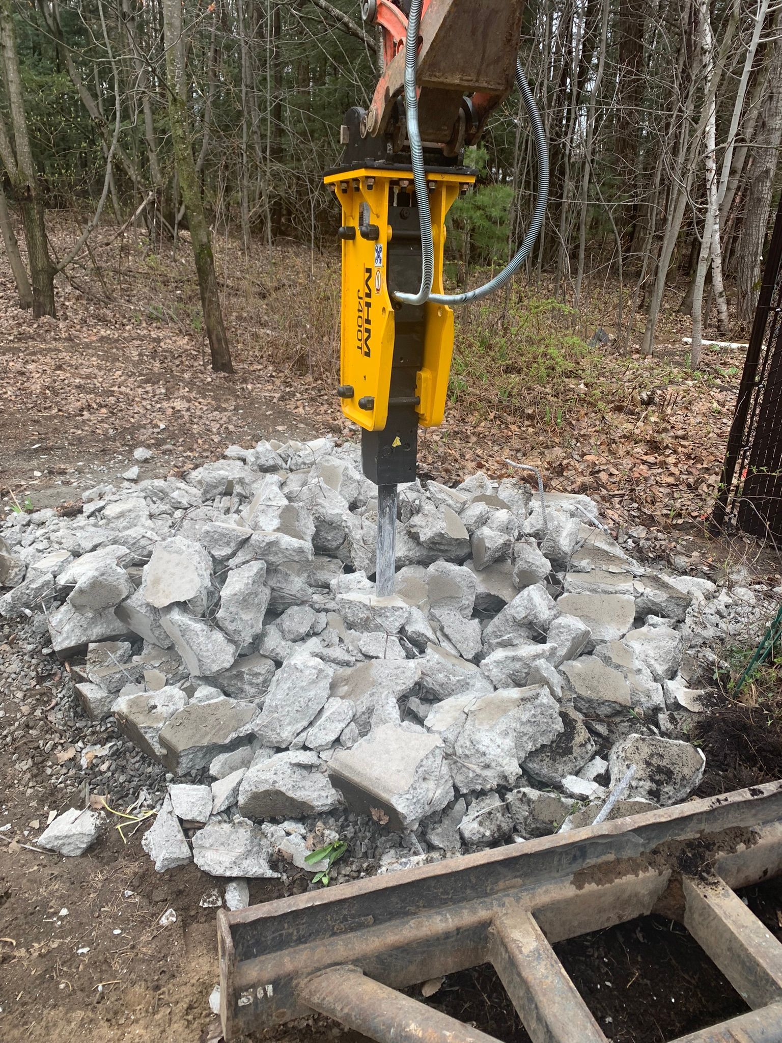 Un marteau hydraulique jaune est posé au sommet d'un tas de roches.