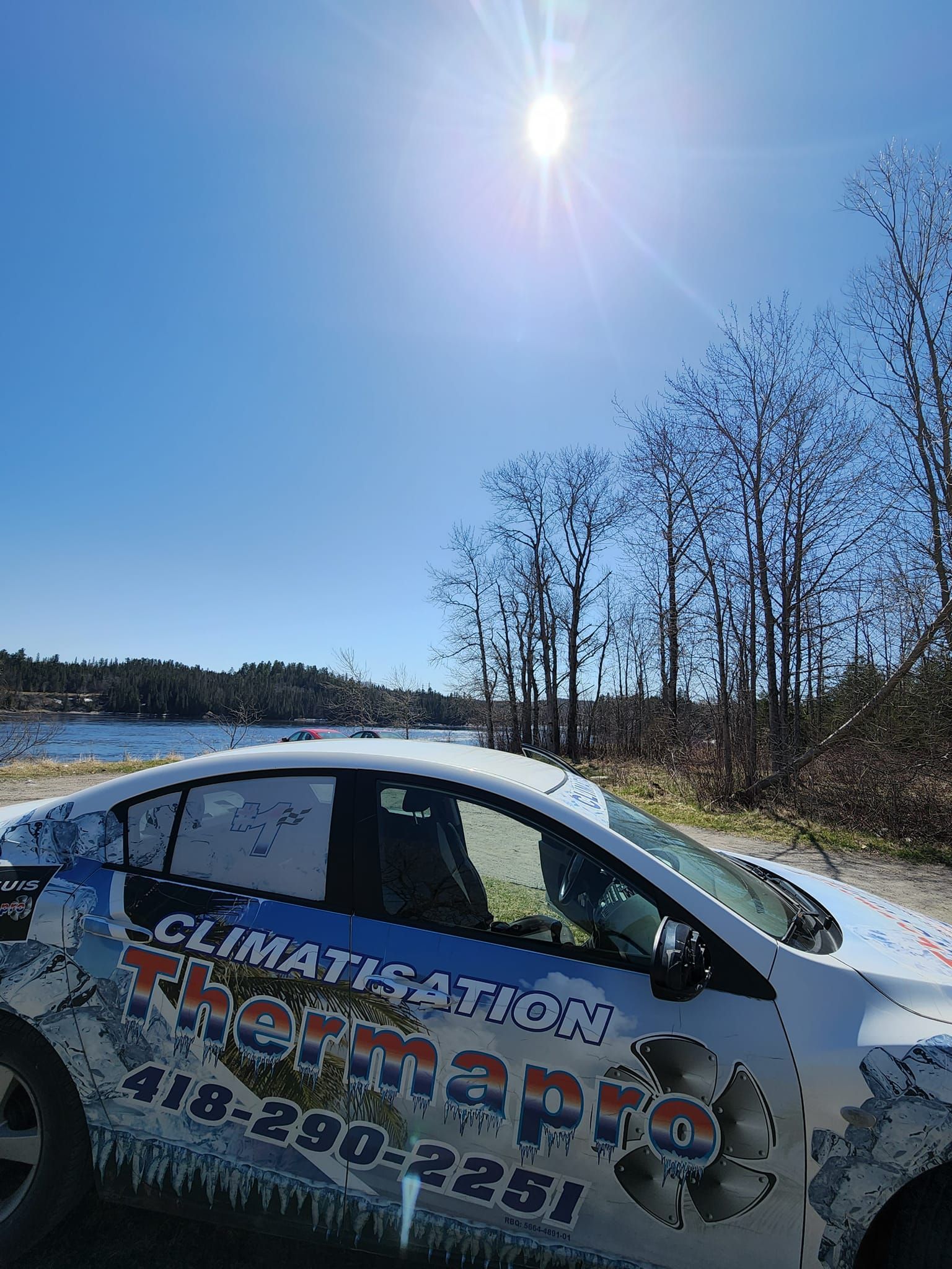 Une voiture blanche est garée sur le bord de la route à côté d'un plan d'eau.
