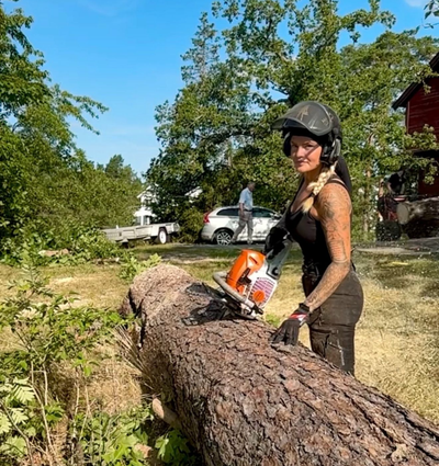 En kvinna sågar ett träd med en motorsåg i skogen.