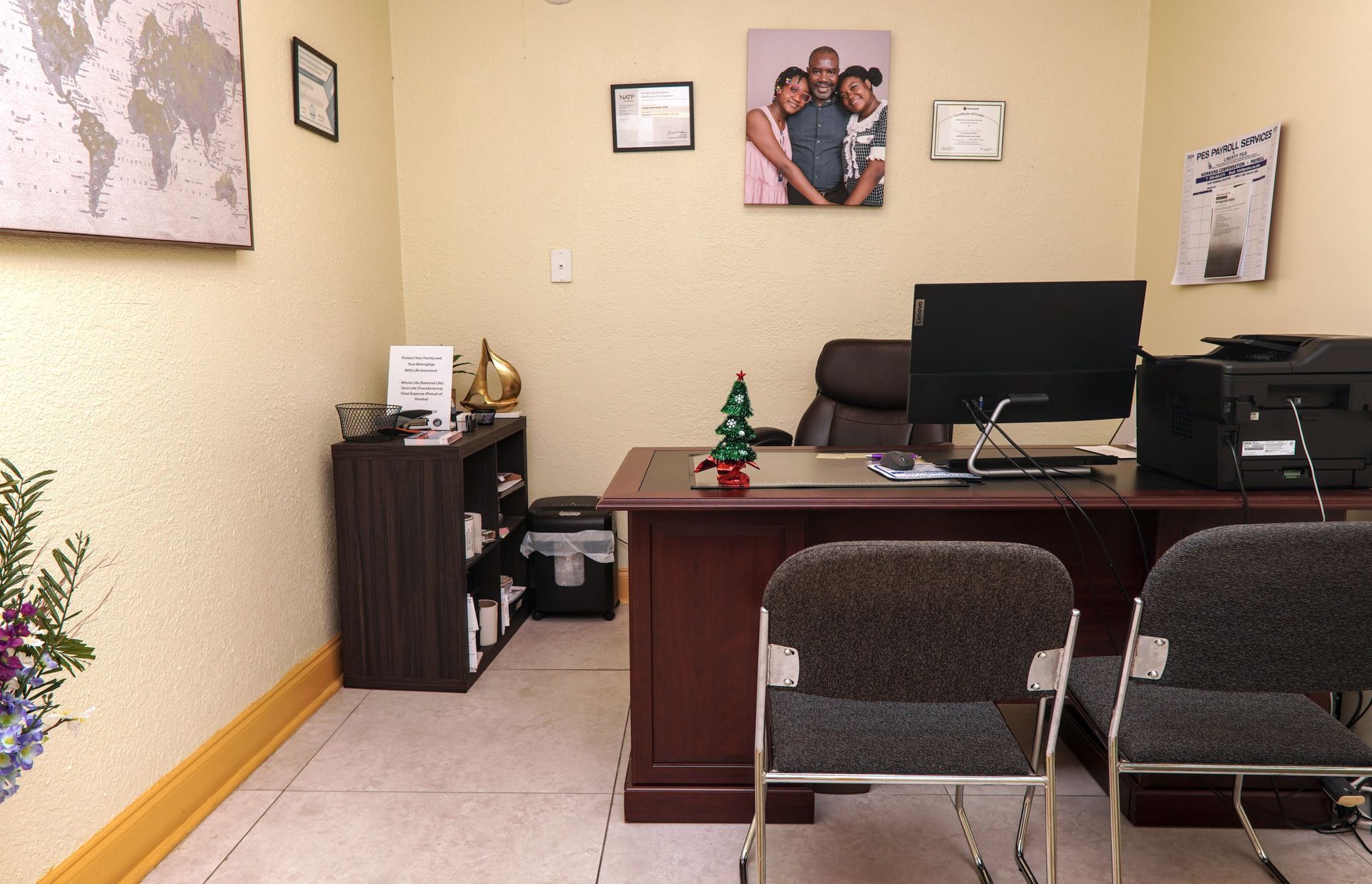 An office with a desk, two chairs, and a family photo on the wall.