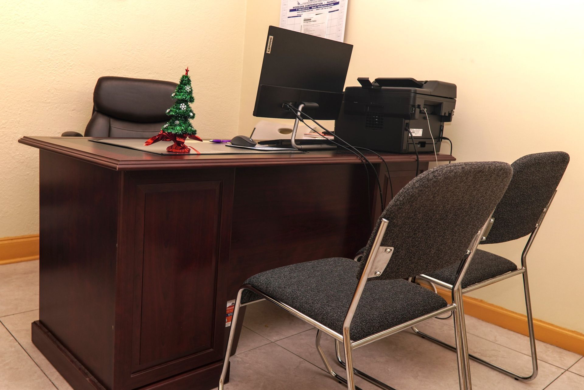 Office desk with a computer, printer, small Christmas tree, and two chairs.