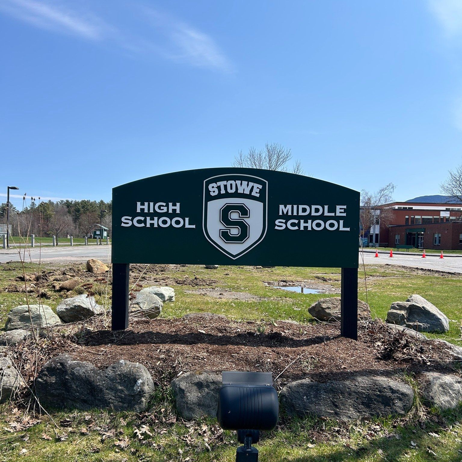 Stowe High School and Middle School sign in front of a green field, under a blue sky.