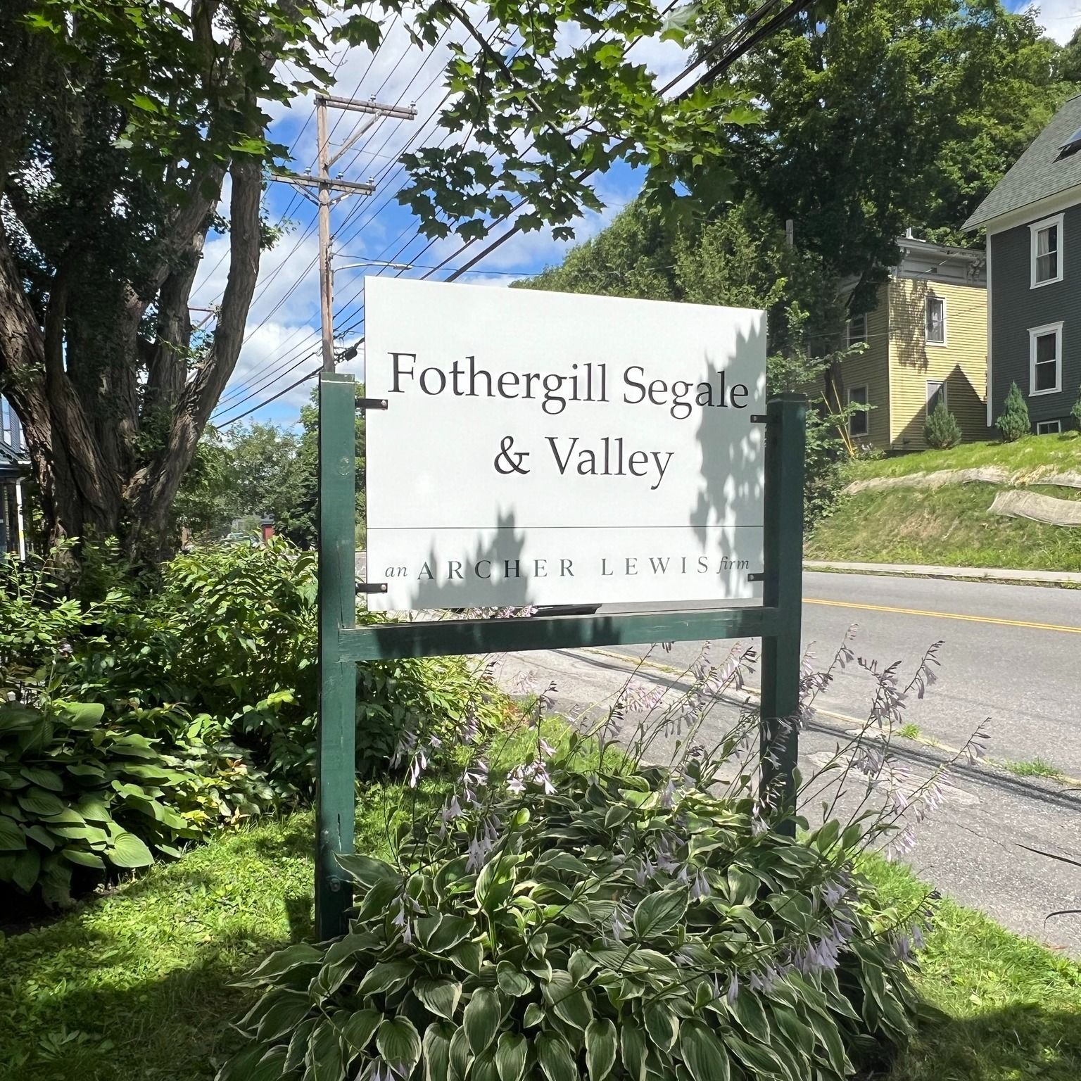 Sign for Fothergill Segale & Valley, on a green post, with greenery in front.