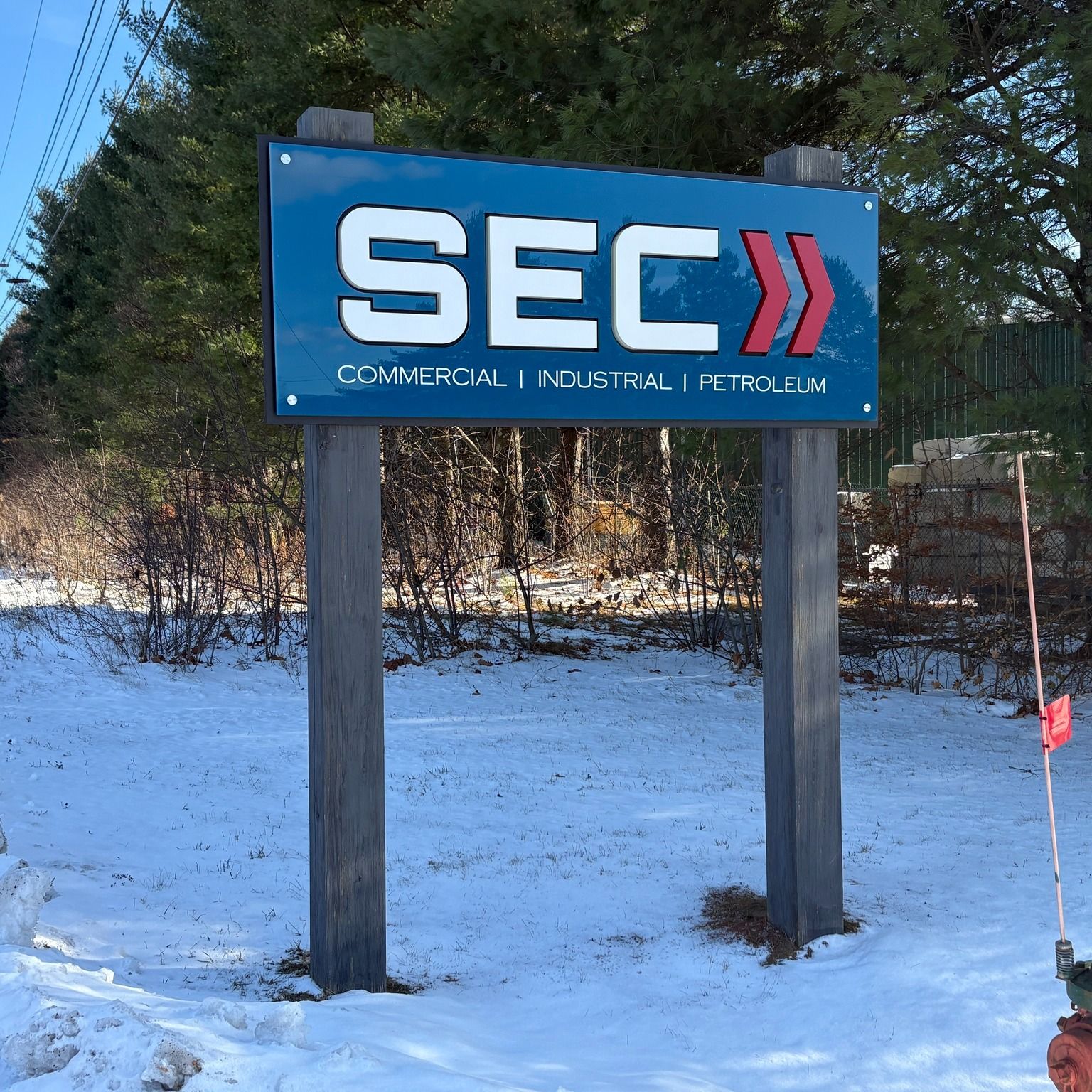 Sign for SEC: blue background, white letters and red arrows in a snowy outdoor setting.