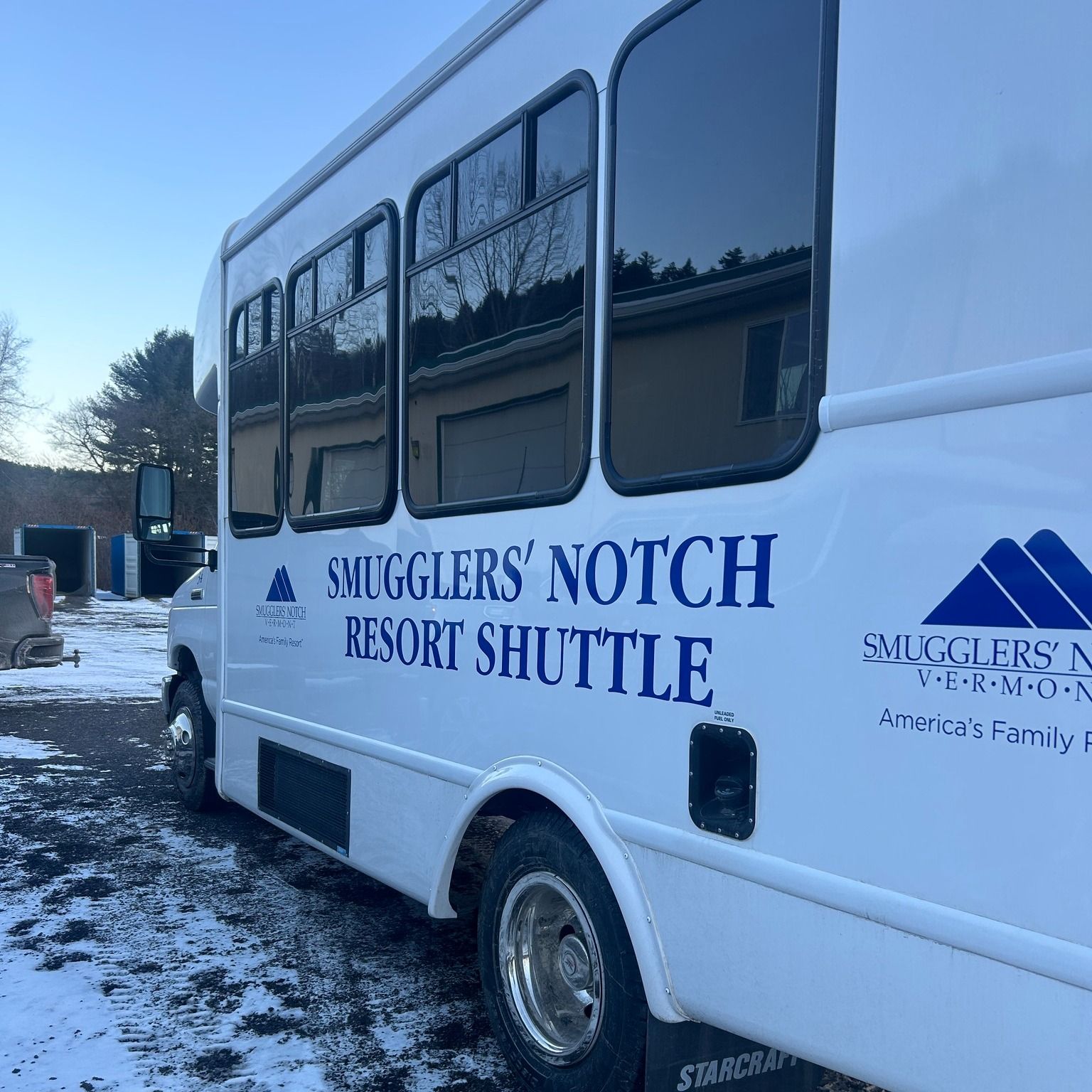White Smugglers' Notch Resort Shuttle bus parked in a snowy area, blue lettering.