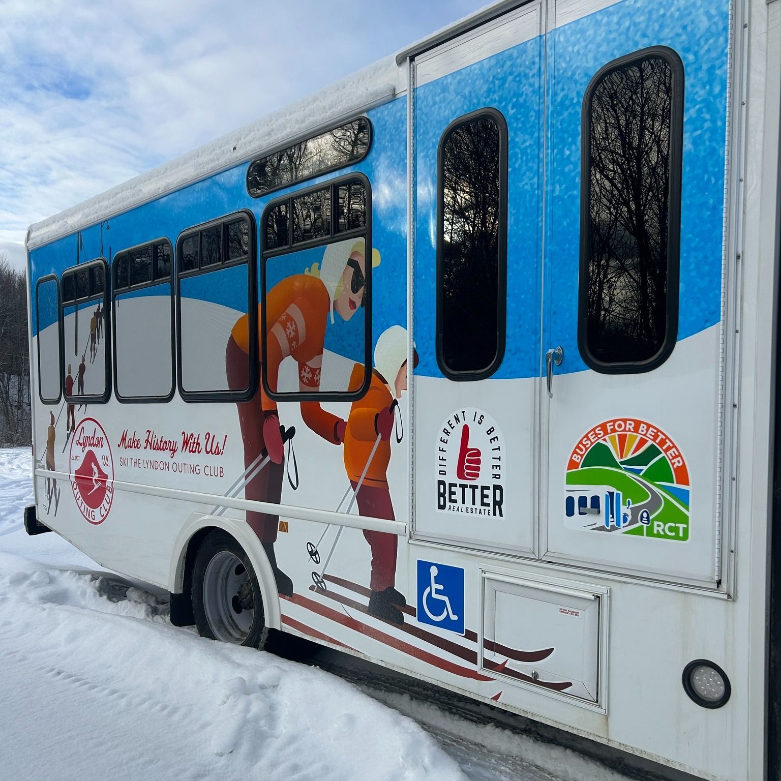 Bus with ski-themed graphics, depicting skiers, a mountain scene, and a wheelchair symbol, parked in snow.