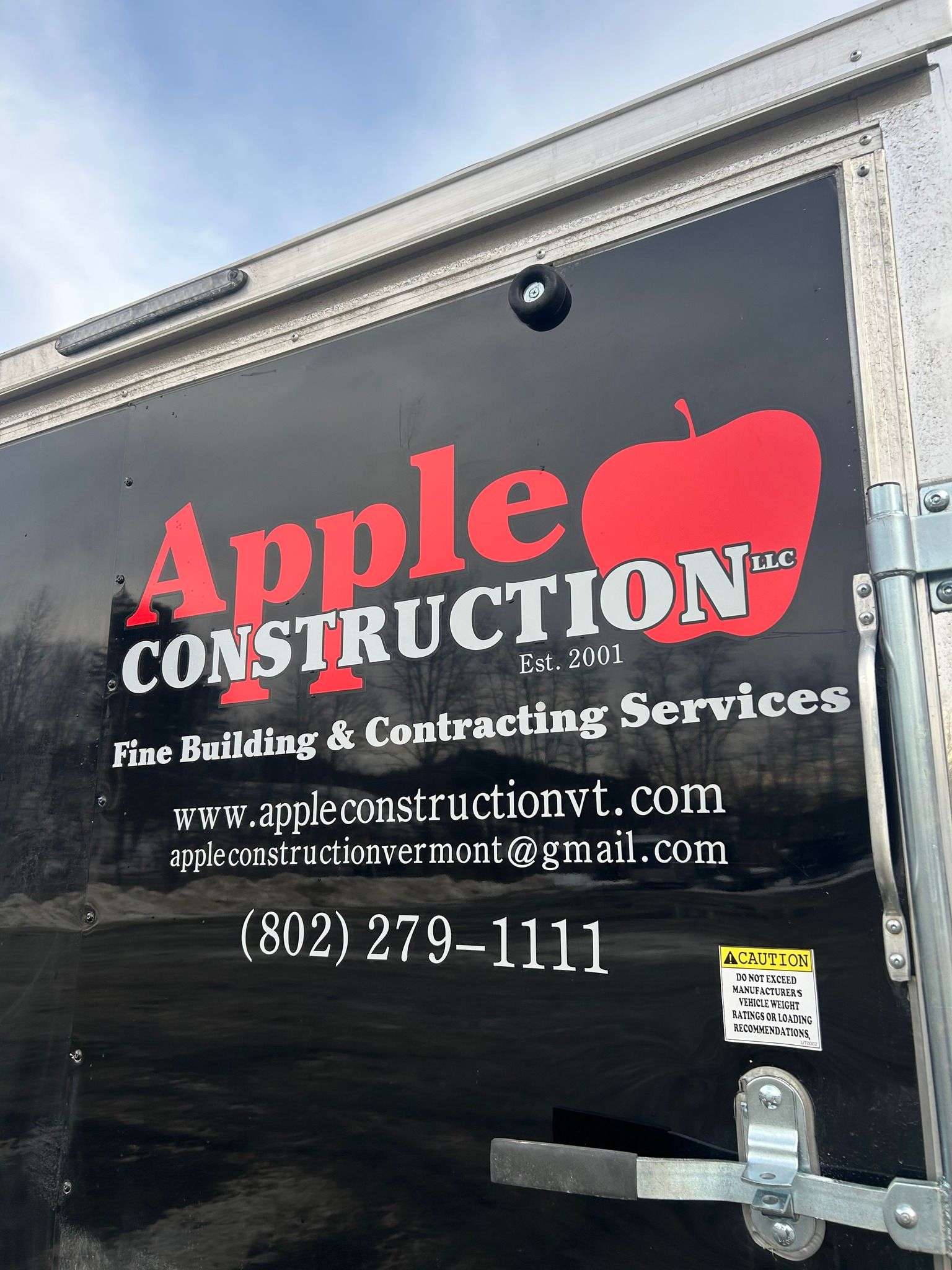 Black Apple Construction trailer with red apple logo, contact info.