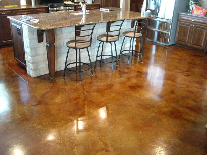 Polished, stained concrete floor in a kitchen, golden-brown with a granite-topped island and bar stools.