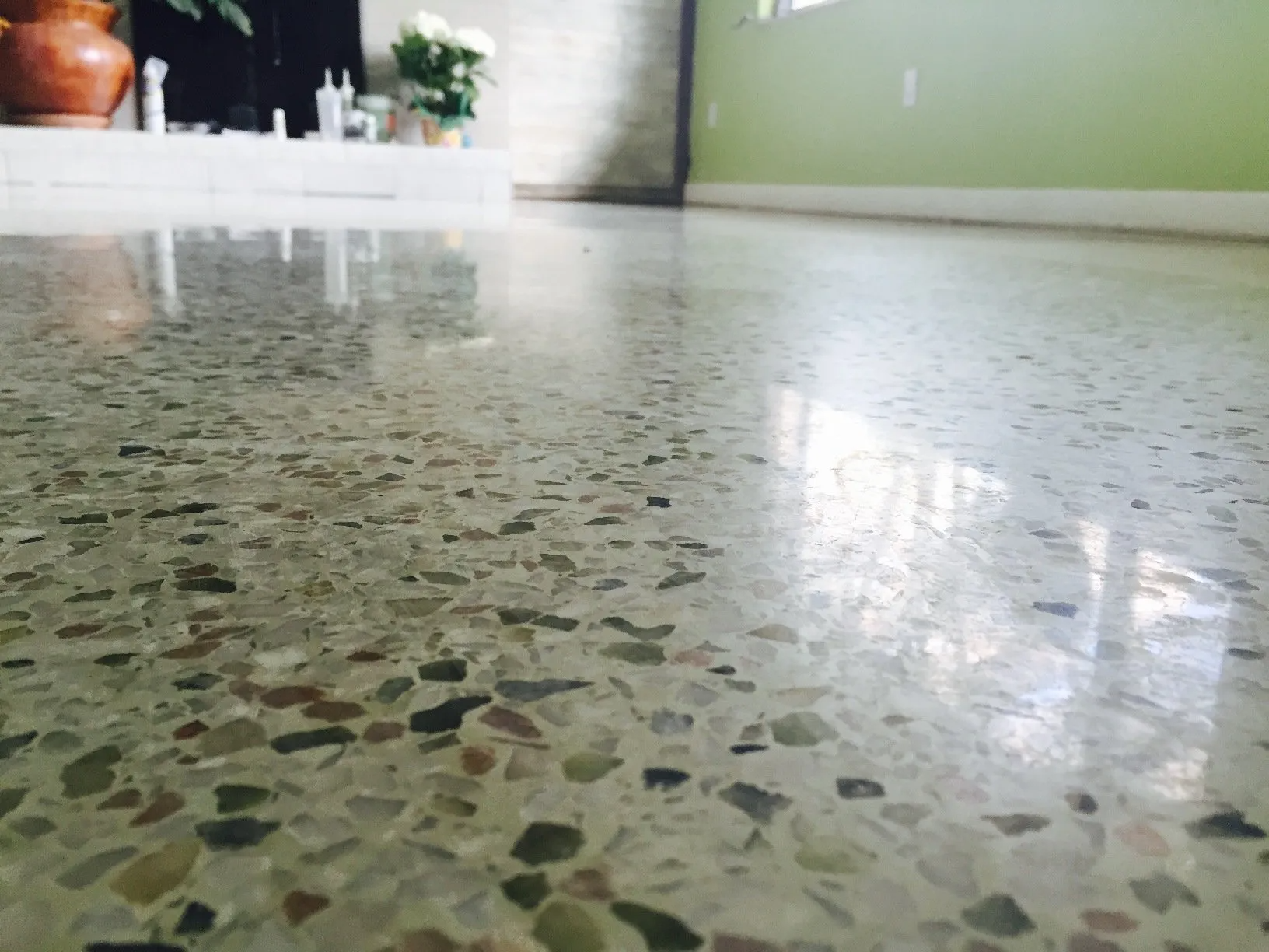 Polished concrete floor with speckled aggregate, reflecting light. In a room with a green wall and fireplace.