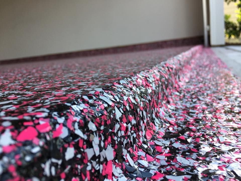 Close-up of a garage floor with a pink, white, and black flake epoxy coating, transitioning onto a slightly raised border.