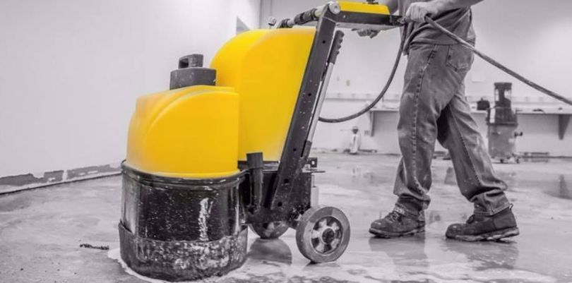 A person using a yellow floor cleaning machine to scrub a wet floor in a commercial setting.