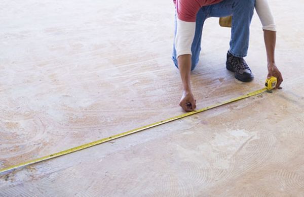 Person kneeling, measuring floor with yellow tape measure.