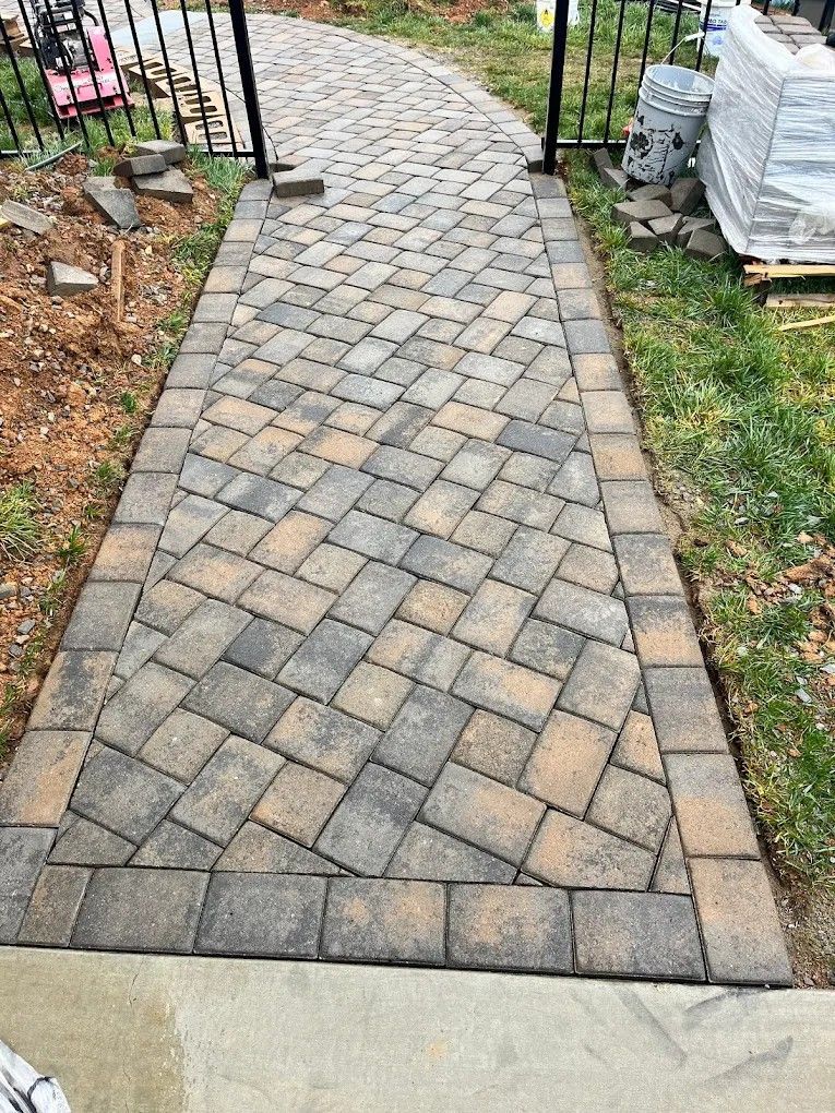 A walkway made of bricks is being built next to a fence.