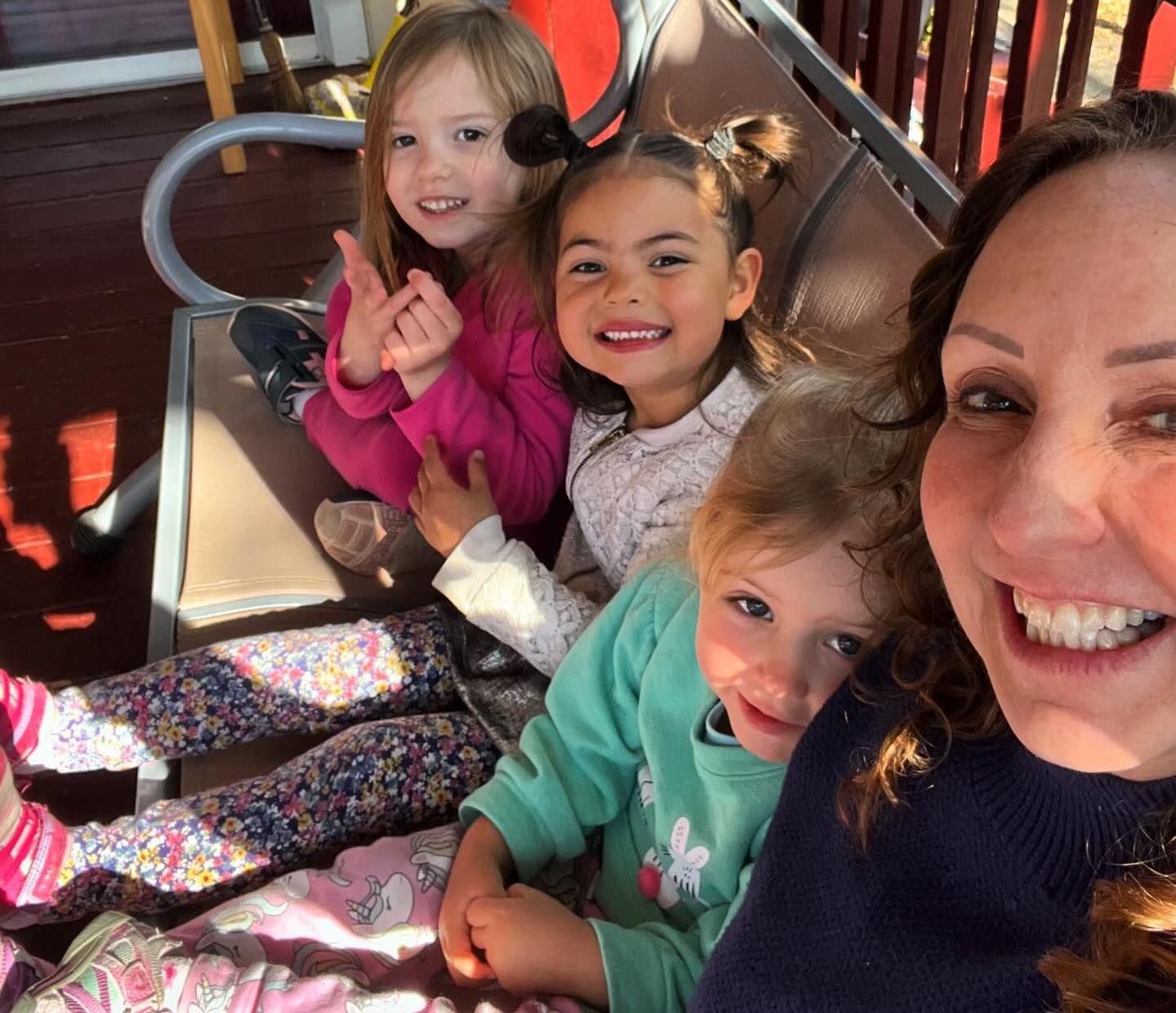A smiling adult taking a selfie with three children on an outdoor swing.