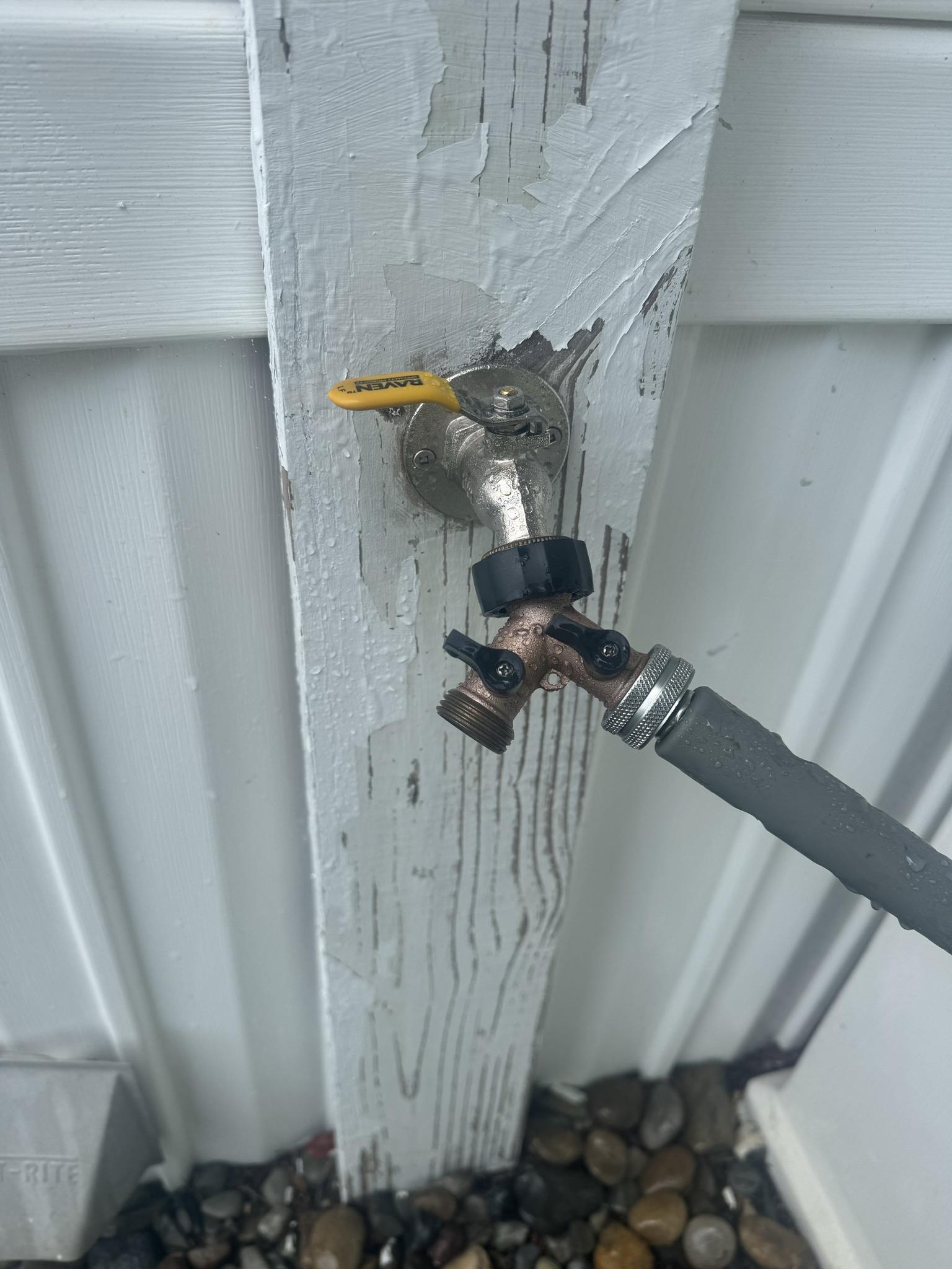 Outdoor faucet on a white wooden post, with a connected gray hose and yellow handle.