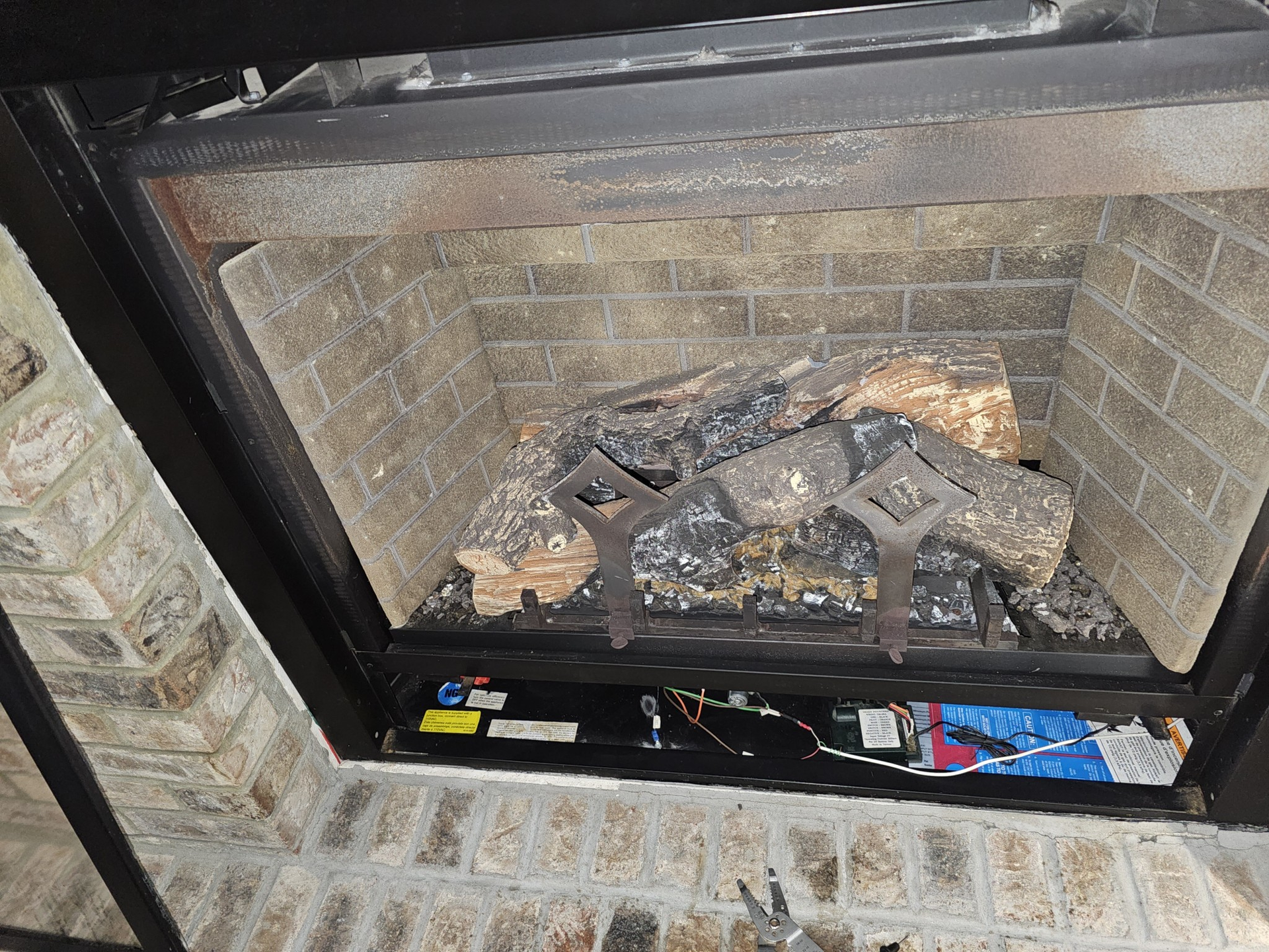 Fireplace interior with brick walls and gas logs. Metal grate and control panel visible.