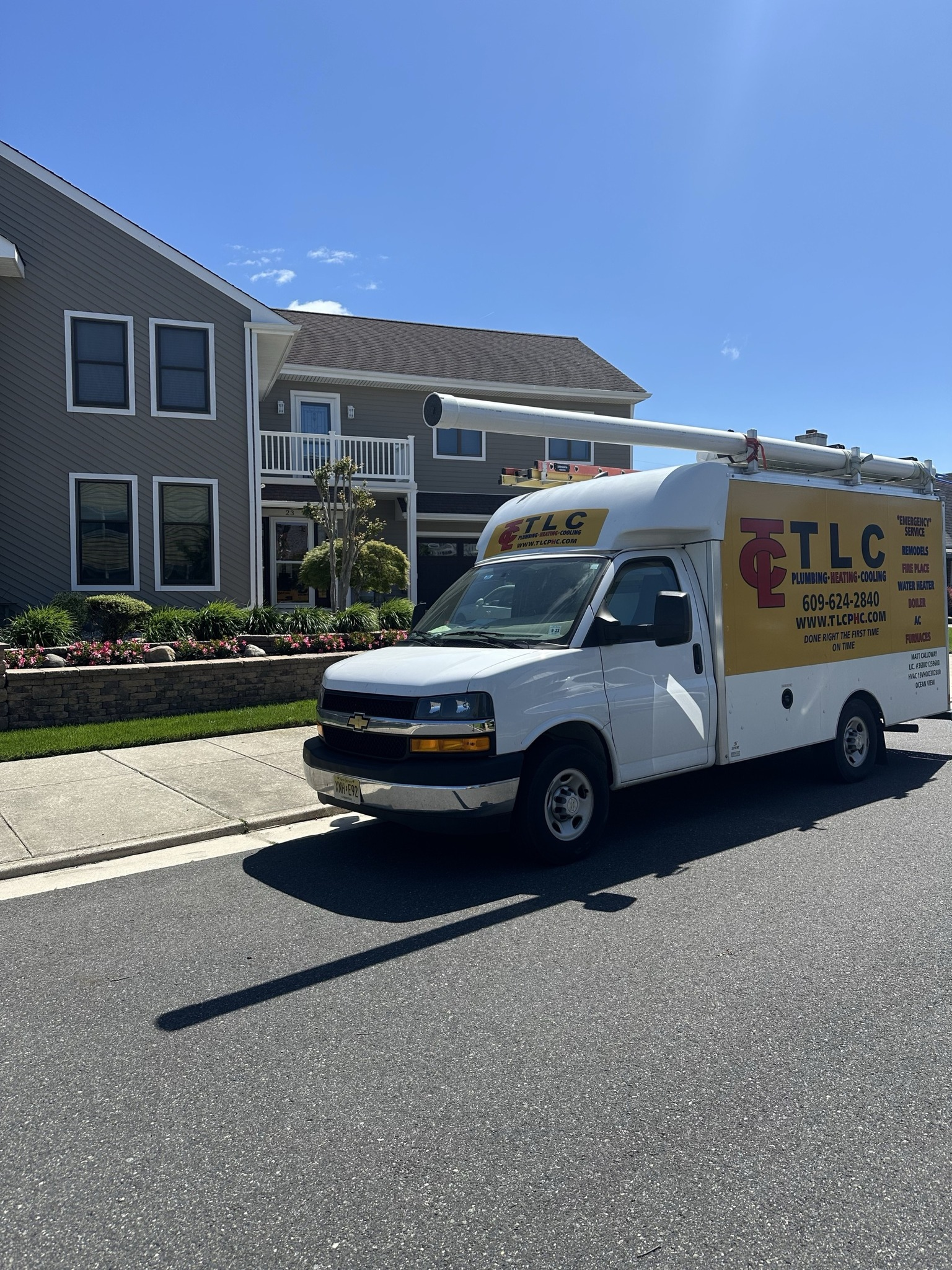 White TLC service van parked on a street in front of a building with a blue sky.
