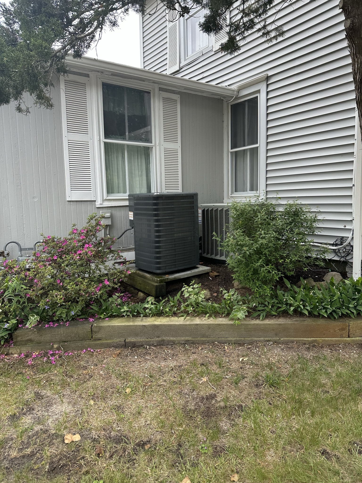 Gray house with window, air conditioner, and bushes in front.