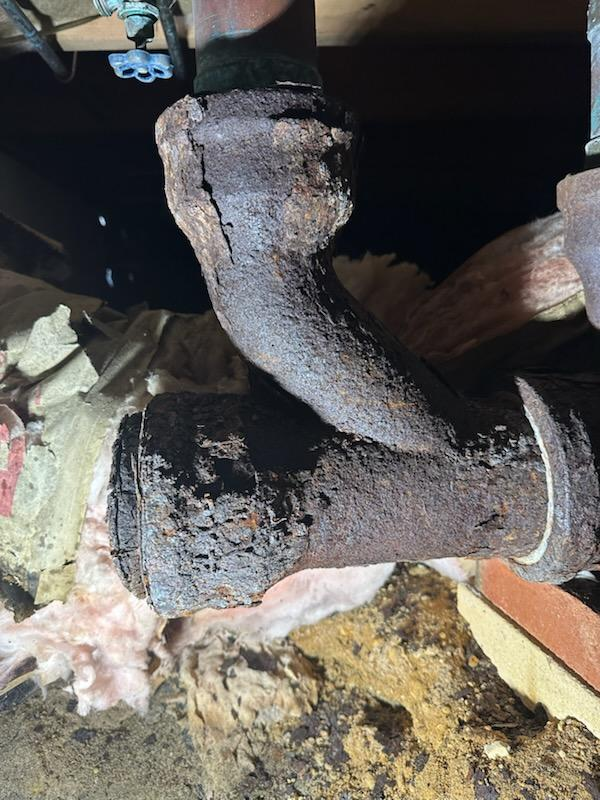 Corroded cast iron pipe in an attic, with visible rust and potential leak.