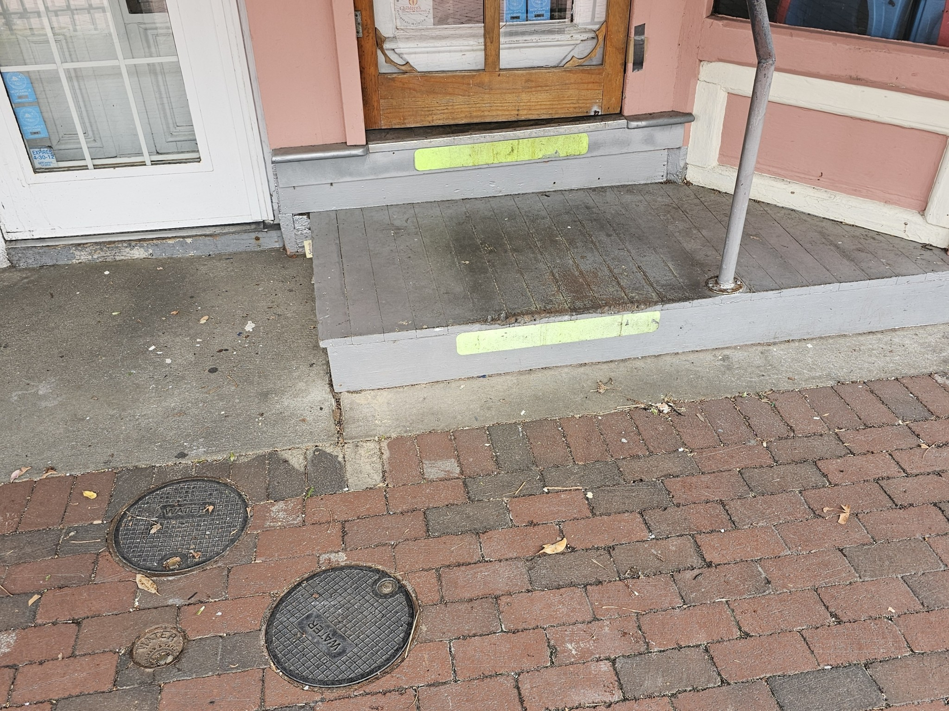 Exterior of a building with a wooden ramp, a door, and brick and concrete sidewalk.