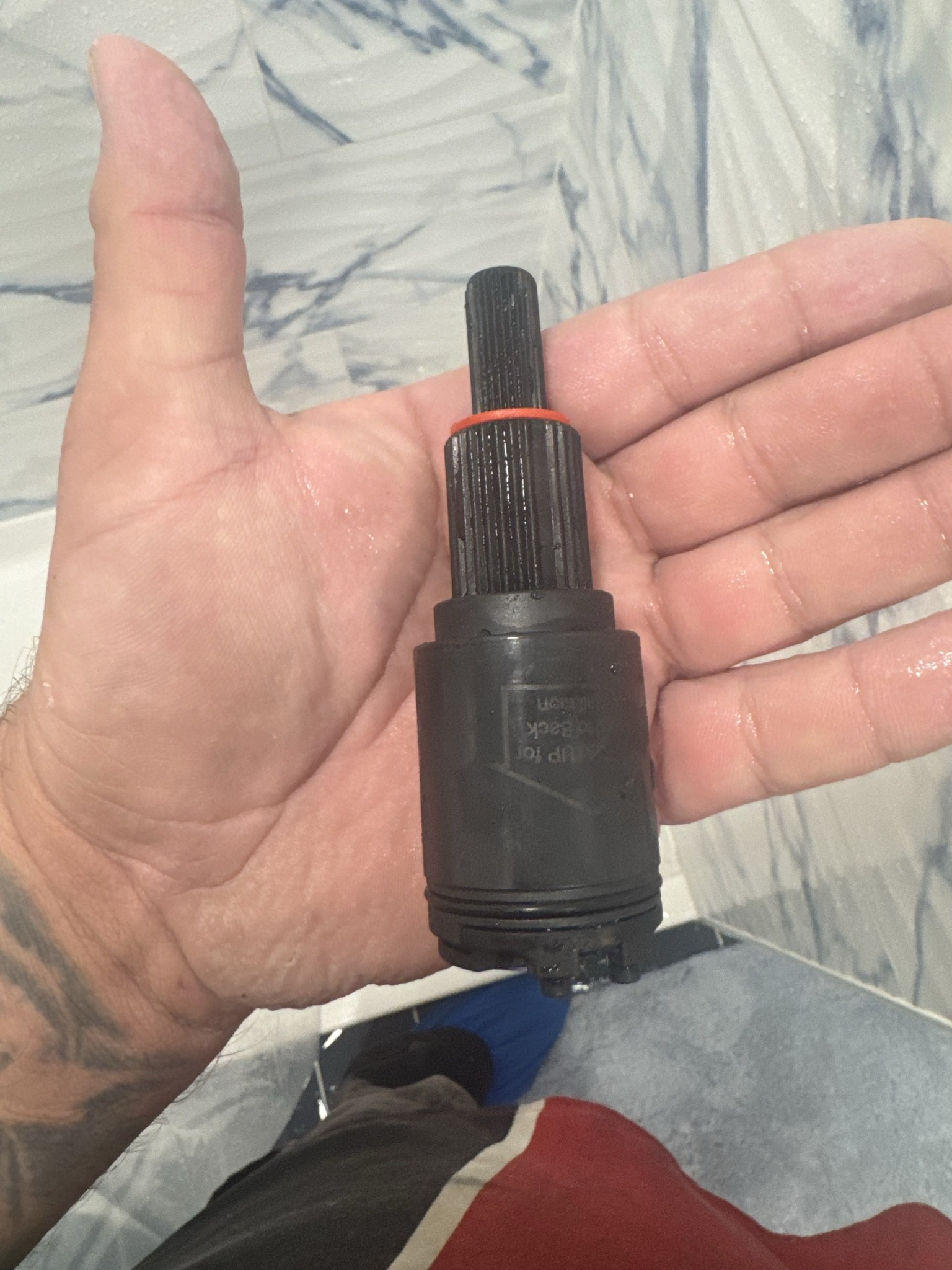 Hand holding a black faucet cartridge, against a light blue tiled wall.