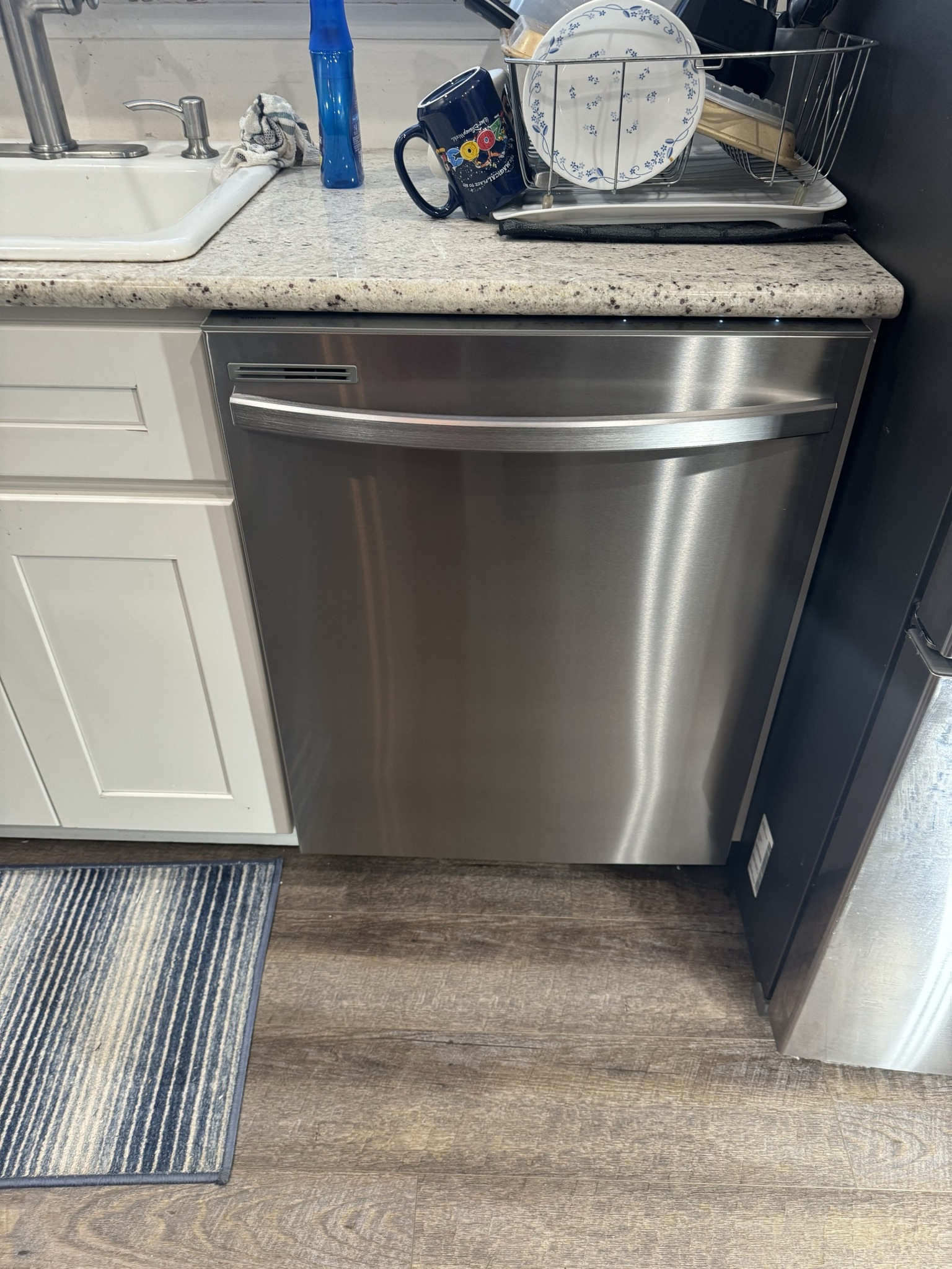 Stainless steel dishwasher in a kitchen, next to white cabinets and countertop.