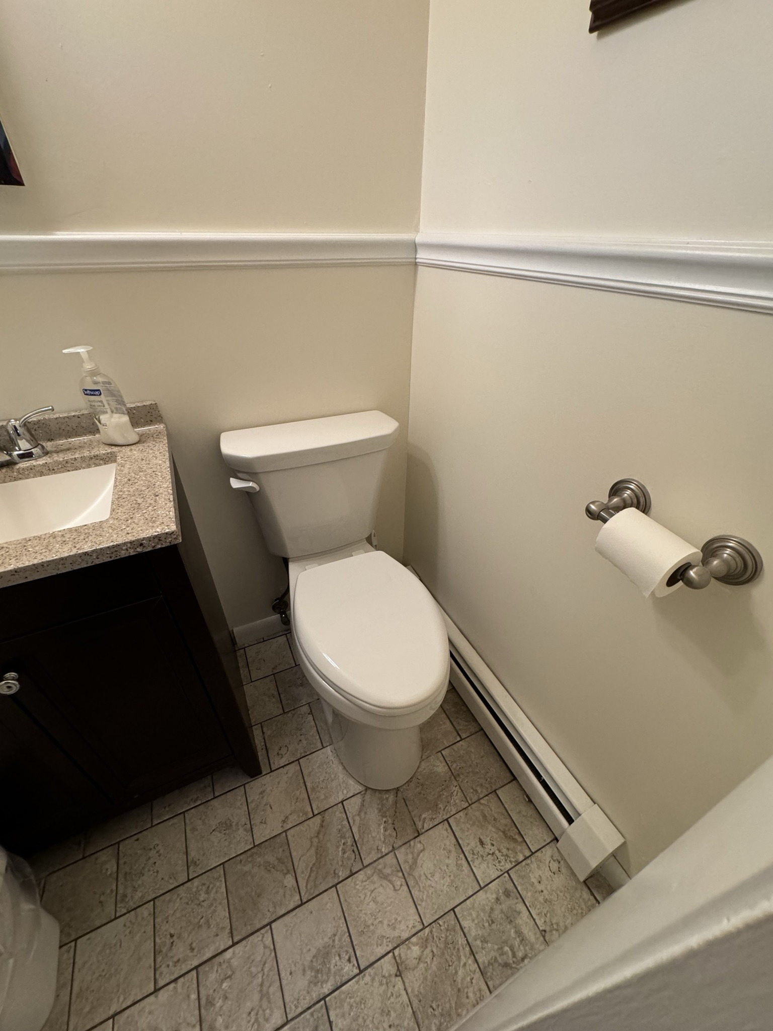 Bathroom with toilet, sink, and tile floor; off-white walls with molding; paper roll holder.